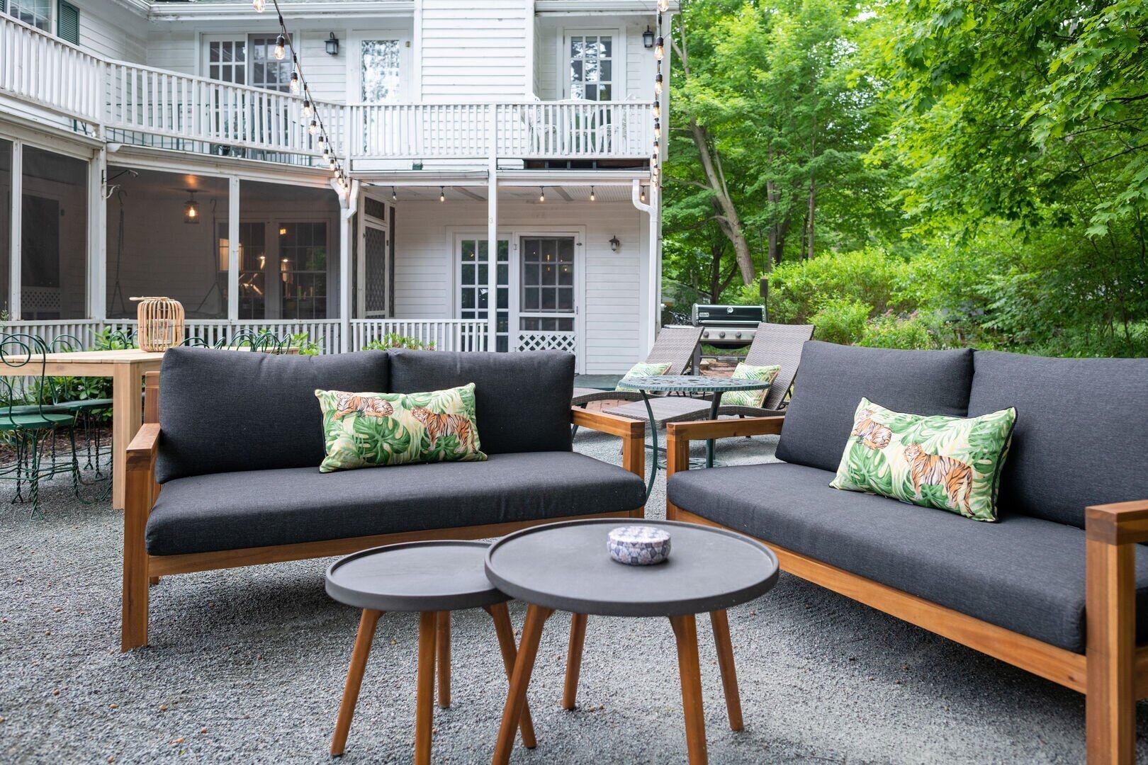A covered outdoor seating area with a sofa and two small tables, surrounded by a white fence and trees.