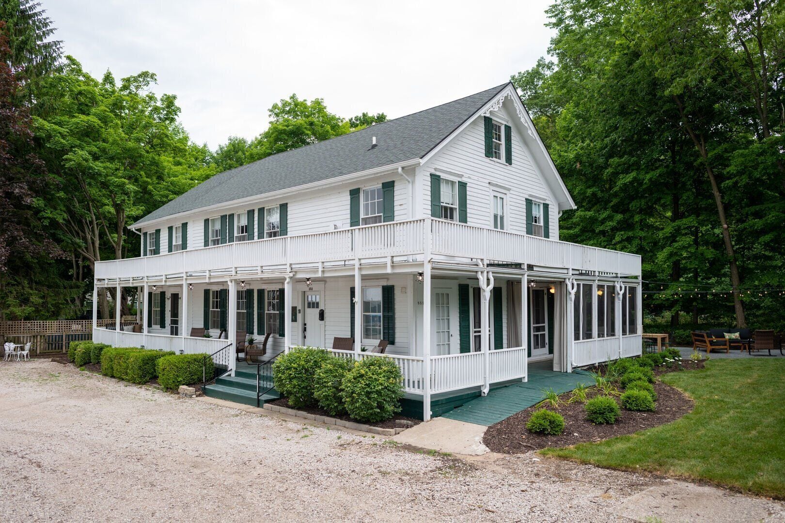 A two-story white house with green shutters, a covered porch, and a gravel driveway.