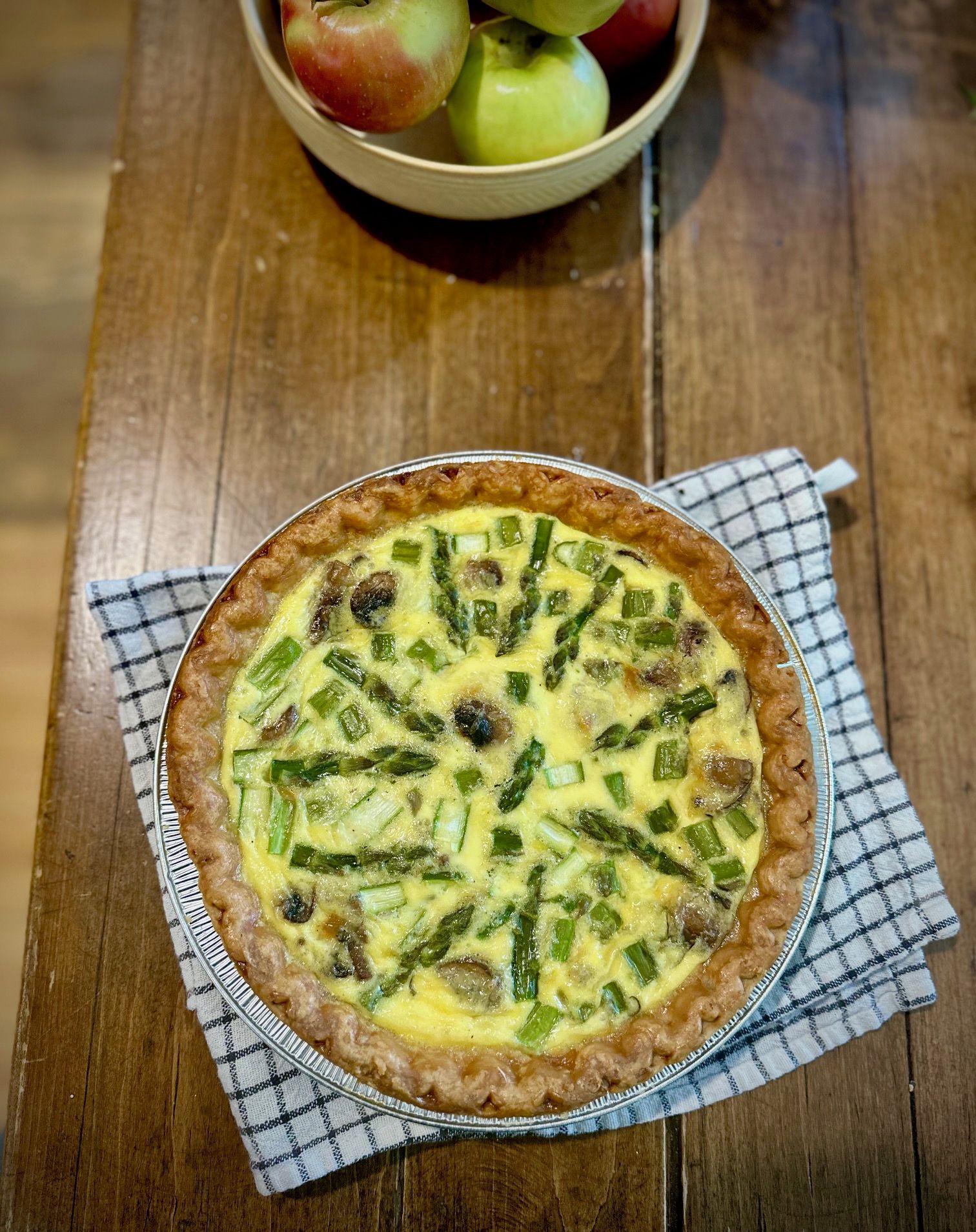 A quiche with green vegetables in a pie dish on a wooden table.