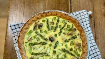 A quiche with green vegetables in a pie dish on a wooden table.