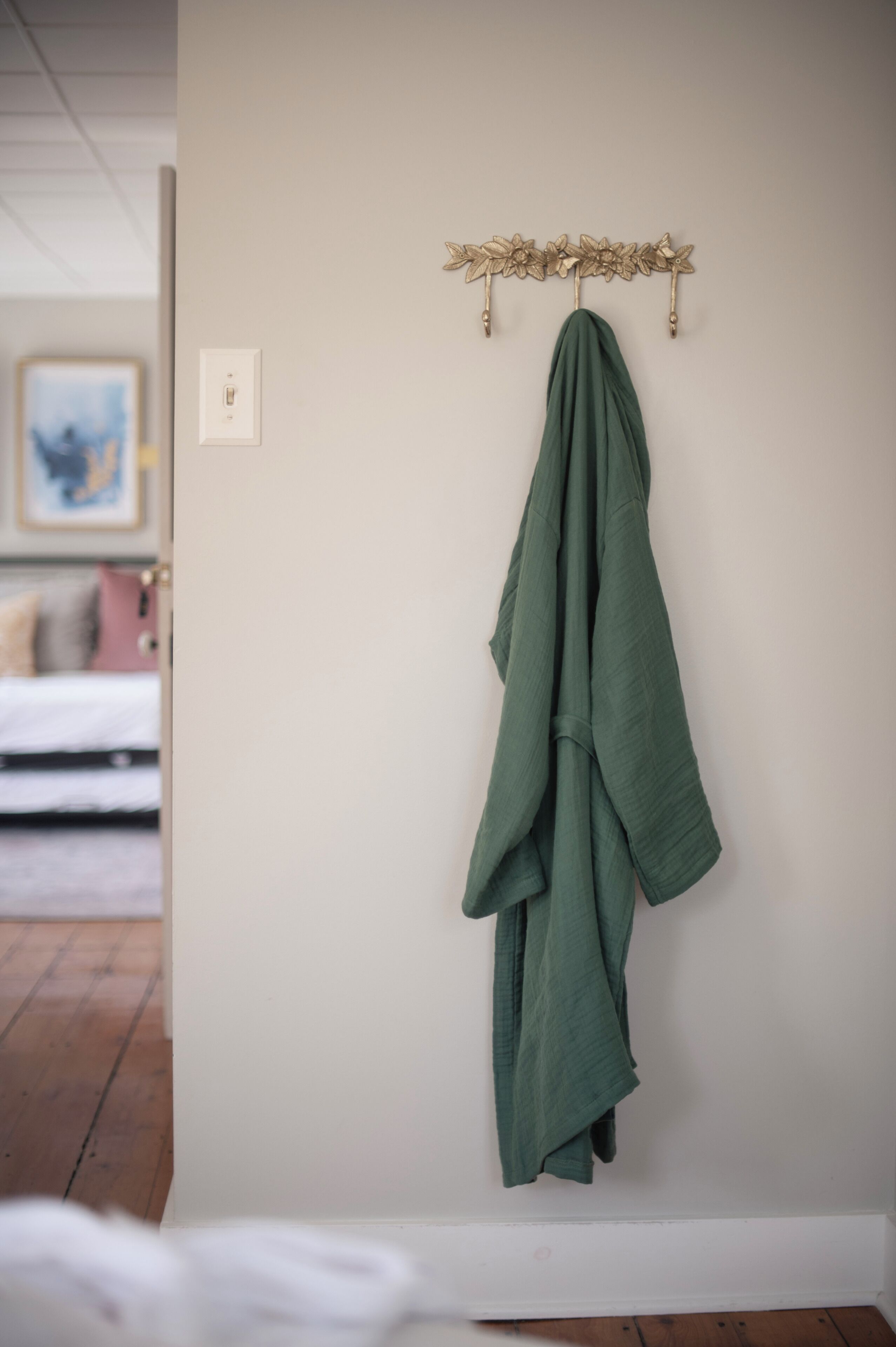 A room with a green towel hanging on a wall-mounted rack, a bed with pillows, and a framed picture on the wall.