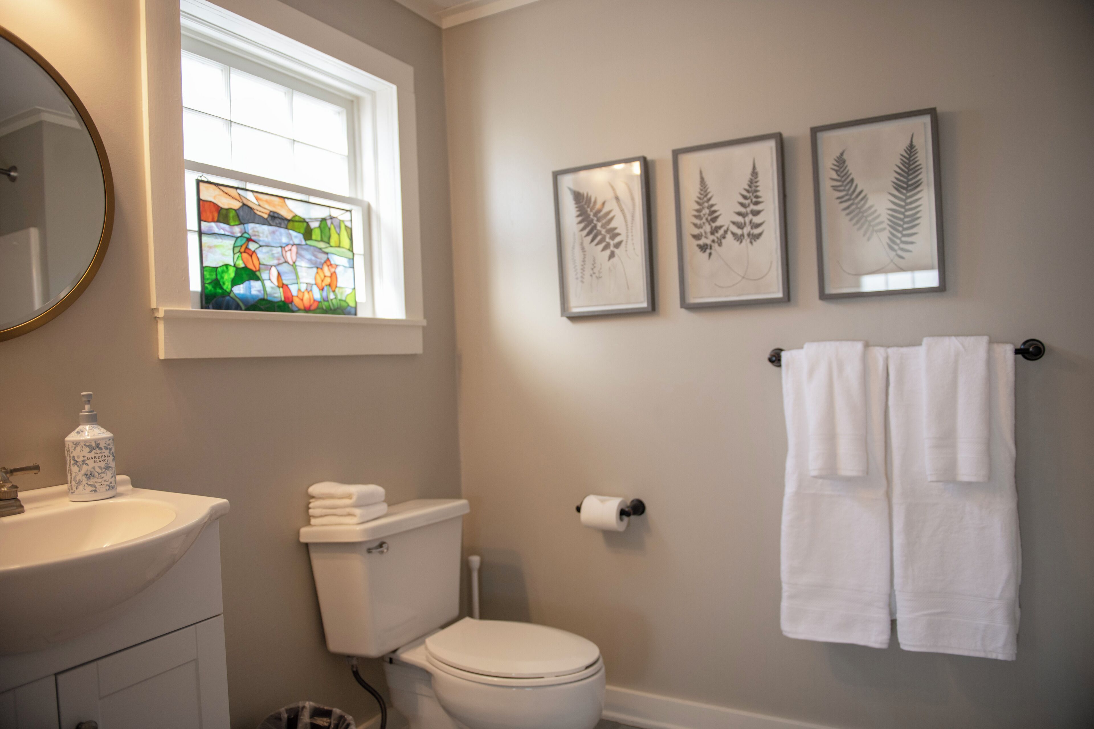 A bathroom with a toilet, sink, and framed leaf artwork on the wall.
