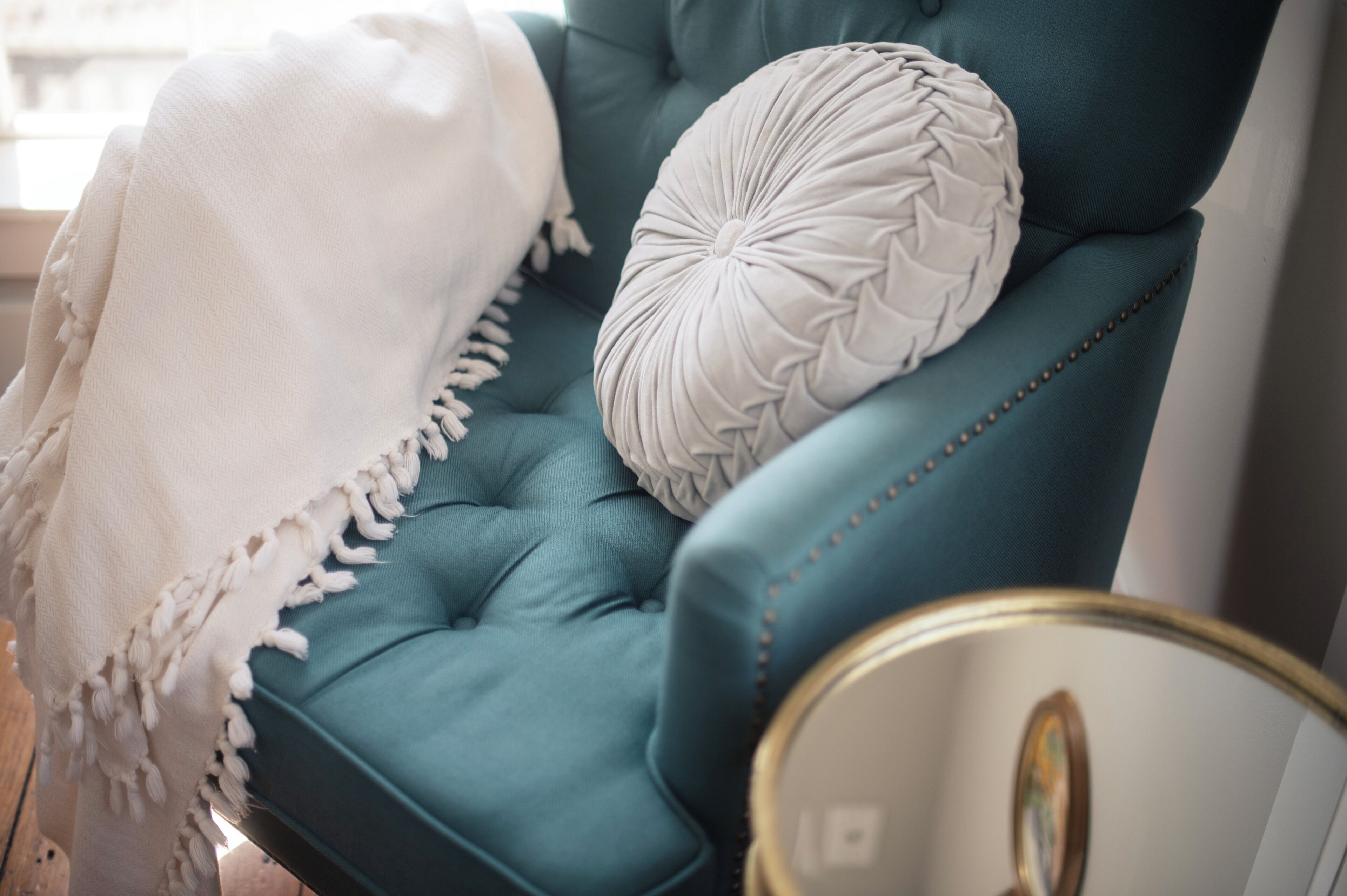 Un fauteuil recouvert d’un tissu turquoise, agrémenté d ’un plaid blanc et d’un coussin décoratif.