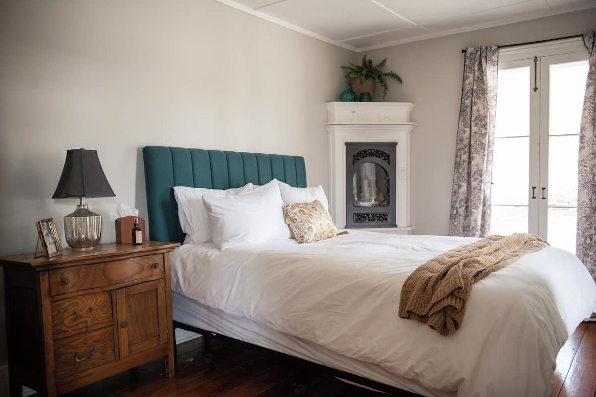 Une chambre à coucher comprenant un lit, une table de chevet, une lampe, une cheminée et une porte avec des rideaux.