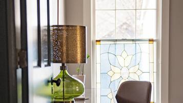 A room with a desk, chair, lamp, and a window with a stained glass design.