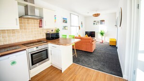 Uma cozinha moderna com forno embutido, um espaço de jantar com mesa e cadeiras de madeira, um sofá e uma TV na sala de estar.