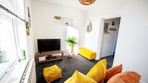 Uma sala de estar com uma televisão, um vaso de planta e um sofá amarelo.