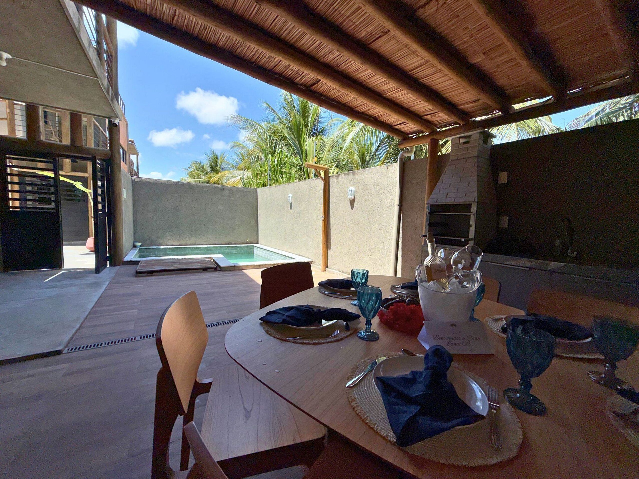 An outdoor dining area with a pool, a grill, and a view of the sky and palm trees.