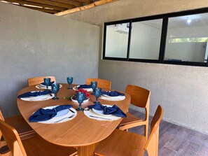 Mesa redonda de madera dispuesta para seis personas, con servilletas azules, platos y vasos.