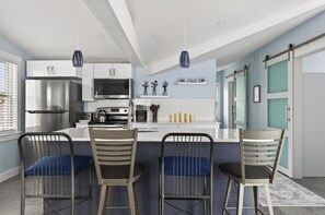 Une cuisine moderne avec des meubles blancs, des appareils en acier inoxydable et un îlot central doté de tabourets de bar.