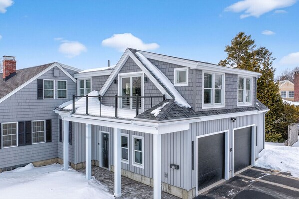 Une maison à deux étages avec un garage, une véranda et un toit recouvert de neige.