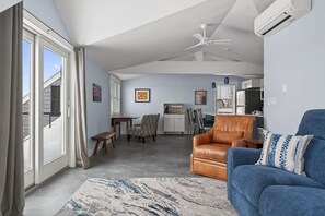 Un salon moderne avec un canapé bleu, un fauteuil en cuir marron, un coin repas avec une table et des chaises, et une cuisine en arrière-plan.