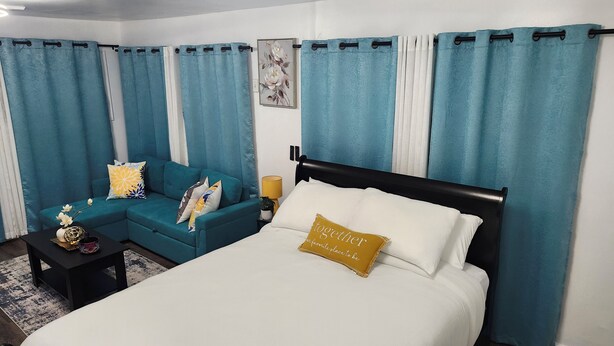 A hotel room with a bed, a sofa, a nightstand, and curtains.