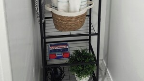 A black metal rack with wooden hangers, a basket of folded towels, and a potted plant.