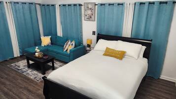 A bedroom with a bed, a sofa, a coffee table, and curtains.