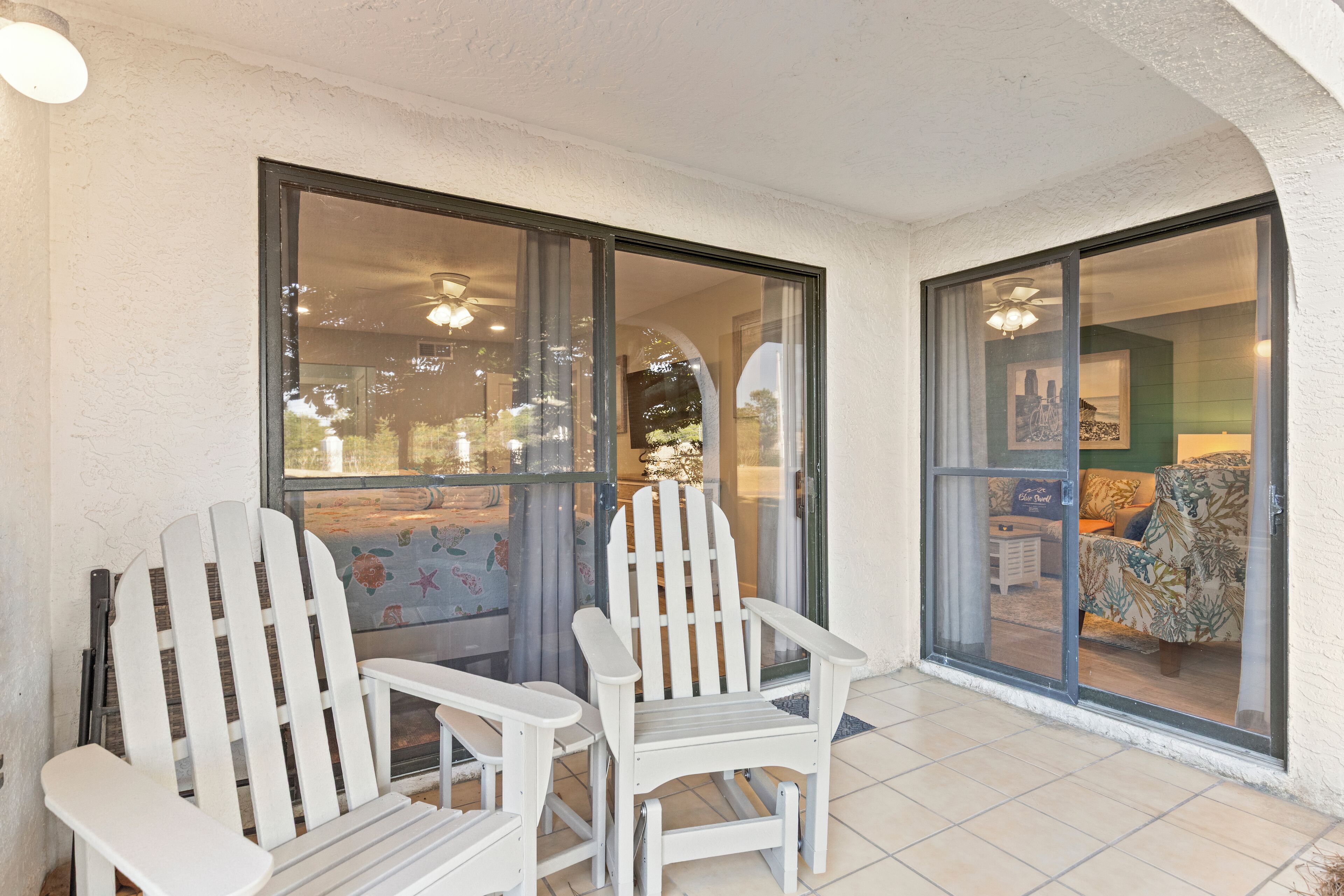 A covered patio area with two Adirondack chairs and a sliding glass door leading to an interior space.