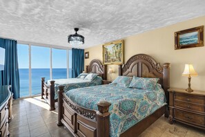A hotel room with a large bed, a smaller bed, a chandelier, a painting, and a view of the sea. - Endless Beach Front Views Await – Long Beach Resort Escape W/Free Beach Chairs (Panama City Beach)