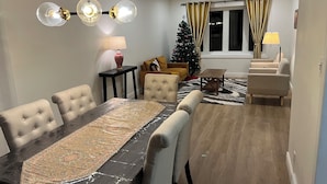 A dining area with a long table, several chairs, a Christmas tree, and a sofa. - Elegant 4BR Home | Private Backyard & Trail Access (Waterloo)
