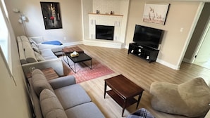 A modern living room with a fireplace, a sofa set, a television, and a coffee table. - Elegant 4BR Home | Private Backyard & Trail Access (Waterloo)