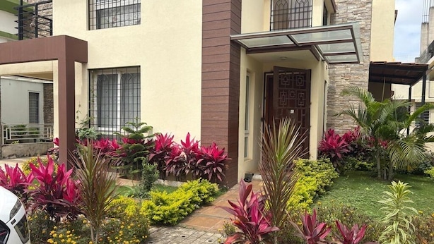 A modern two-story house with a well-maintained garden featuring vibrant plants and a paved driveway.
