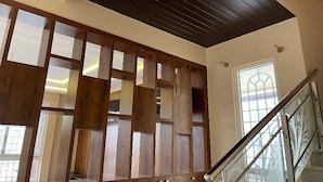 A spacious interior with a high ceiling, a staircase with glass railings, and a large window providing natural light.