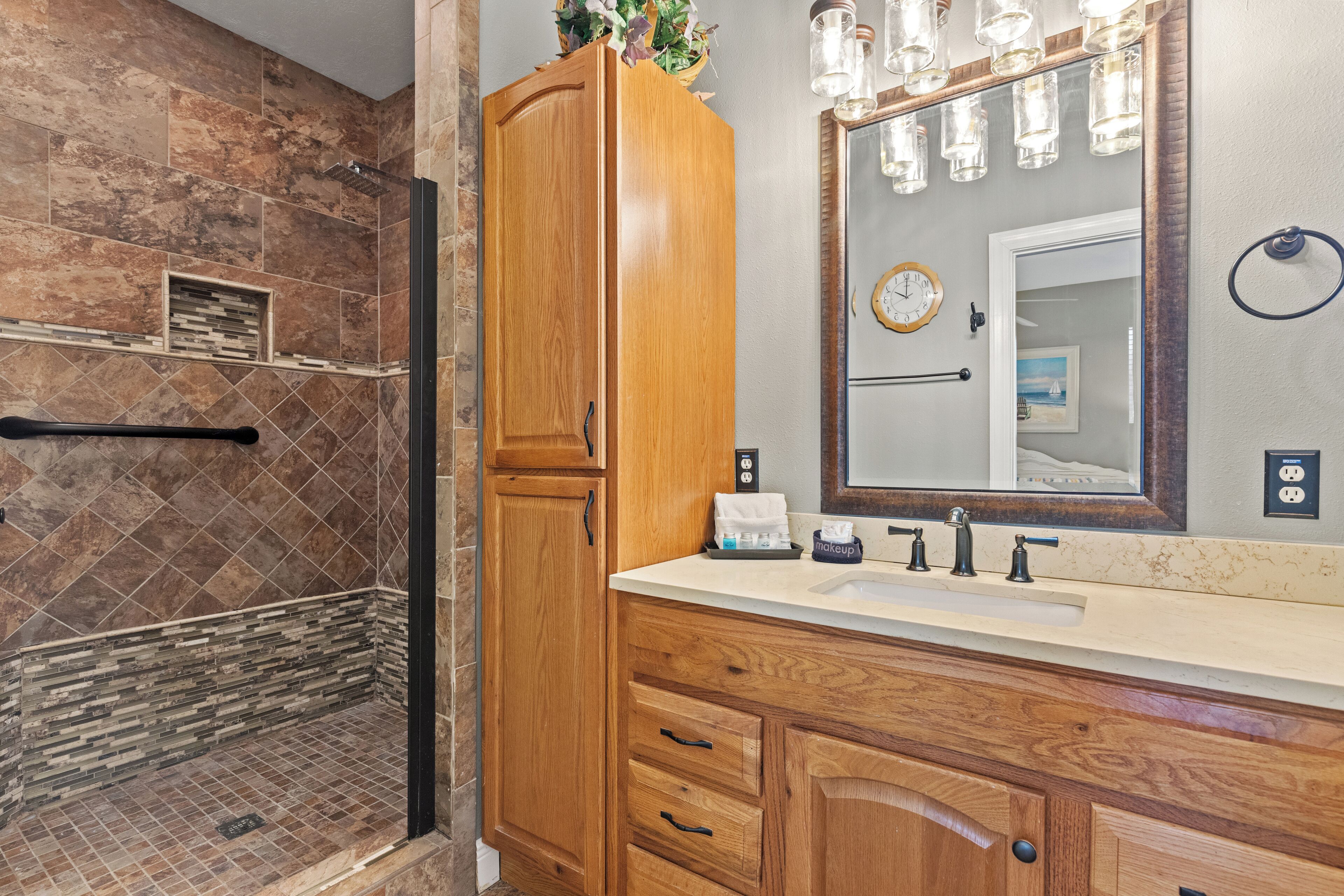 A bathroom with a shower, wooden vanity, and a large mirror with lights.