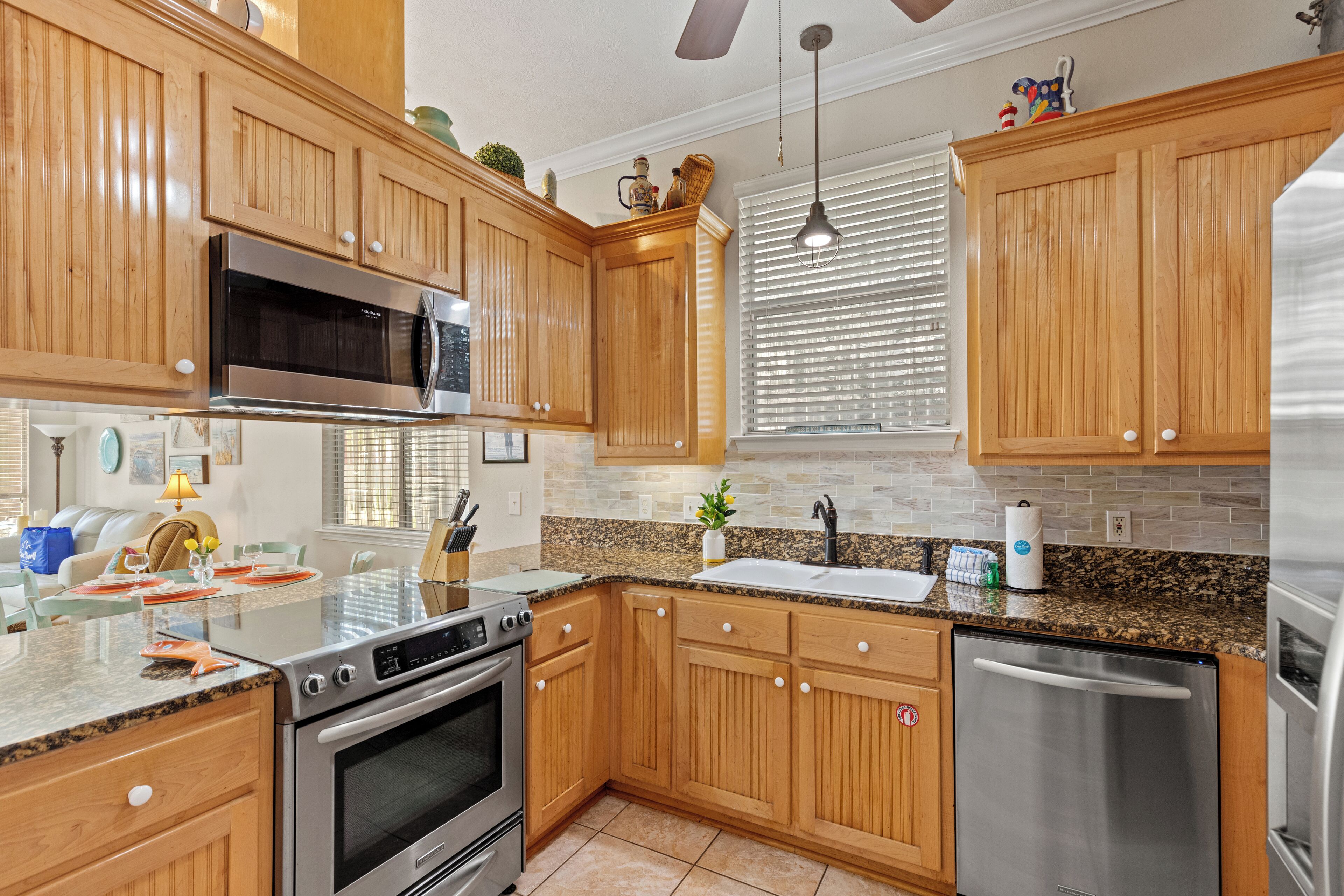 A kitchen with wooden cabinets, stainless steel appliances, a granite countertop, and a window with blinds.