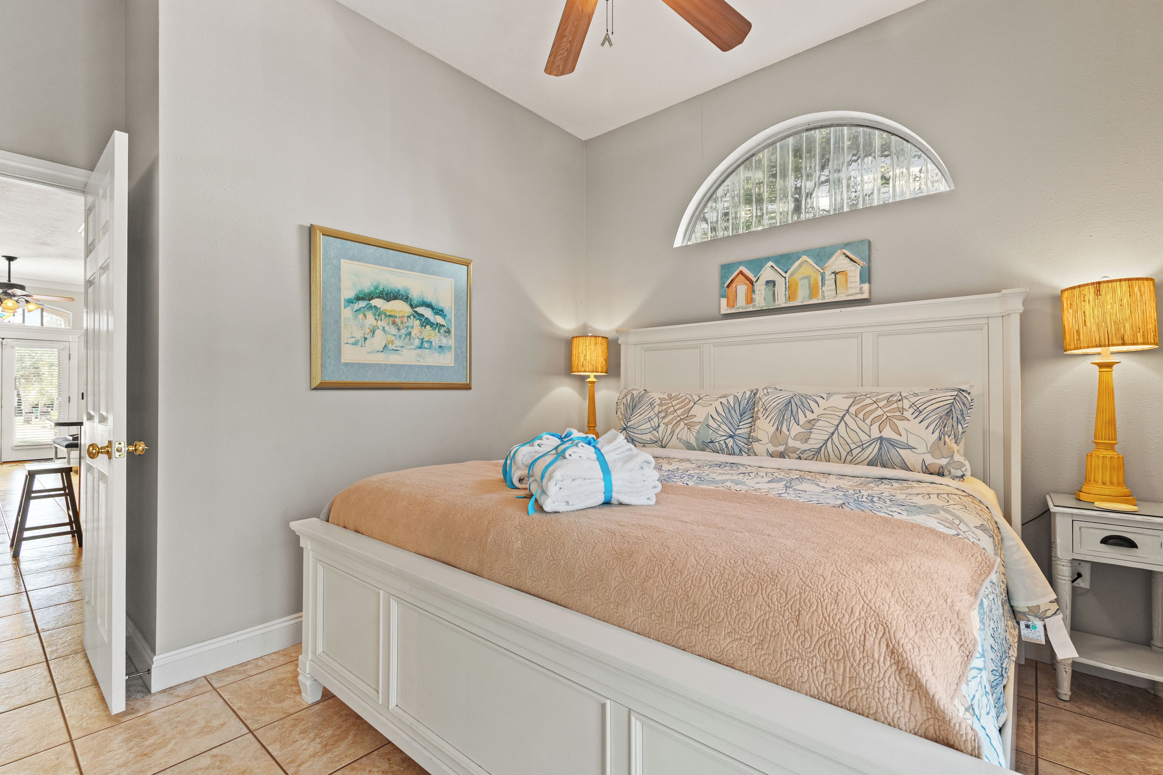 A bedroom with a bed, two bedside lamps, a painting, and a window with a mirror.