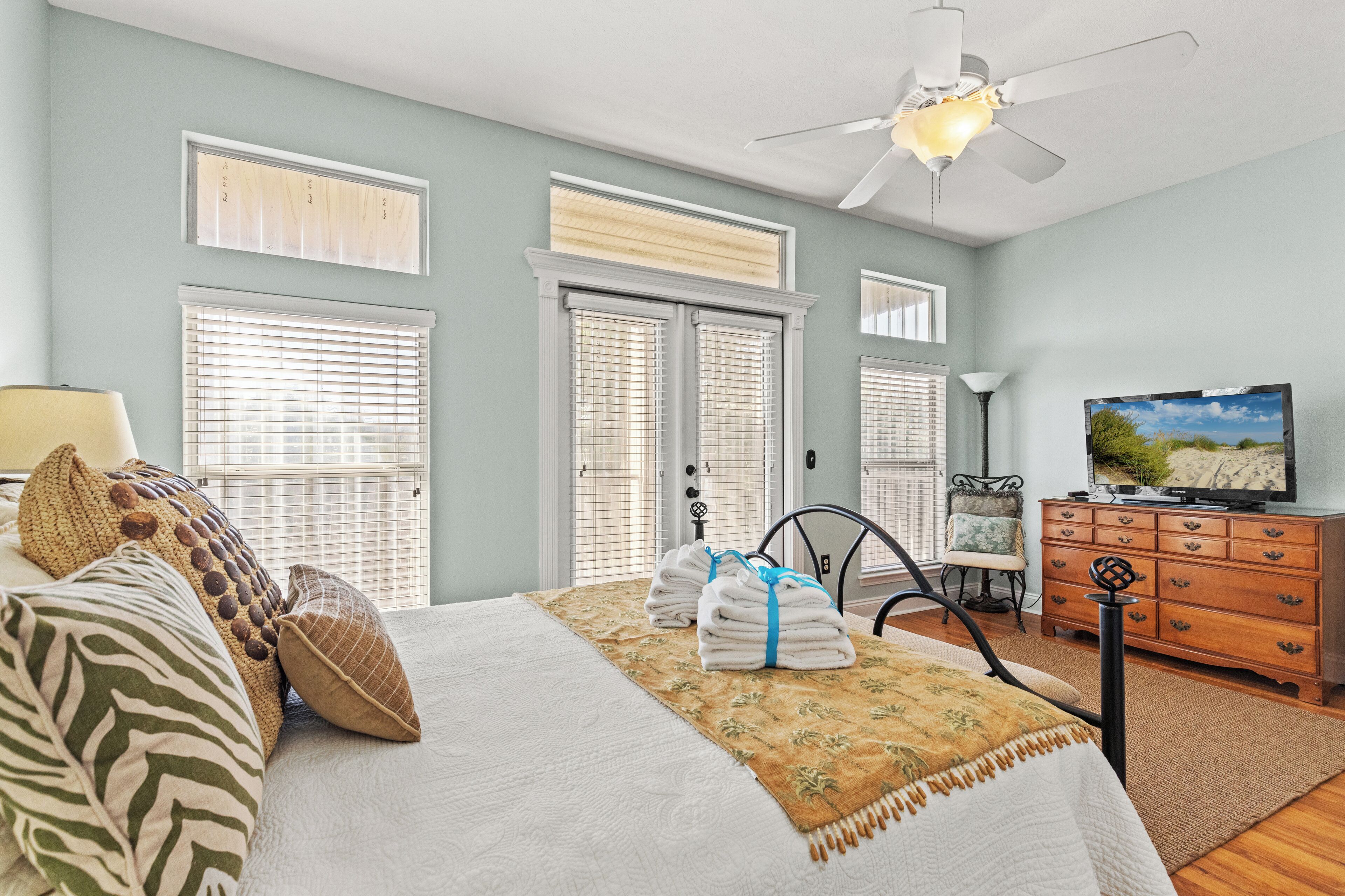 A bedroom with a bed, a television, a dresser, and a ceiling fan.