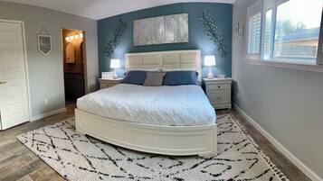 Een slaapkamer met een groot bed, twee nachtkastjes met lampen, een decoratief wandobject en uitzicht buiten door een raam.