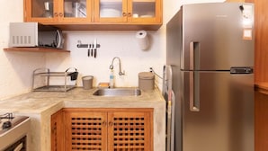 A compact kitchen with wooden cabinets, a stainless steel refrigerator, a microwave, and a sink with a faucet. - MHV Milagres - Casa da Villa 08, Casa em Villa (Passo de Camaragibe)