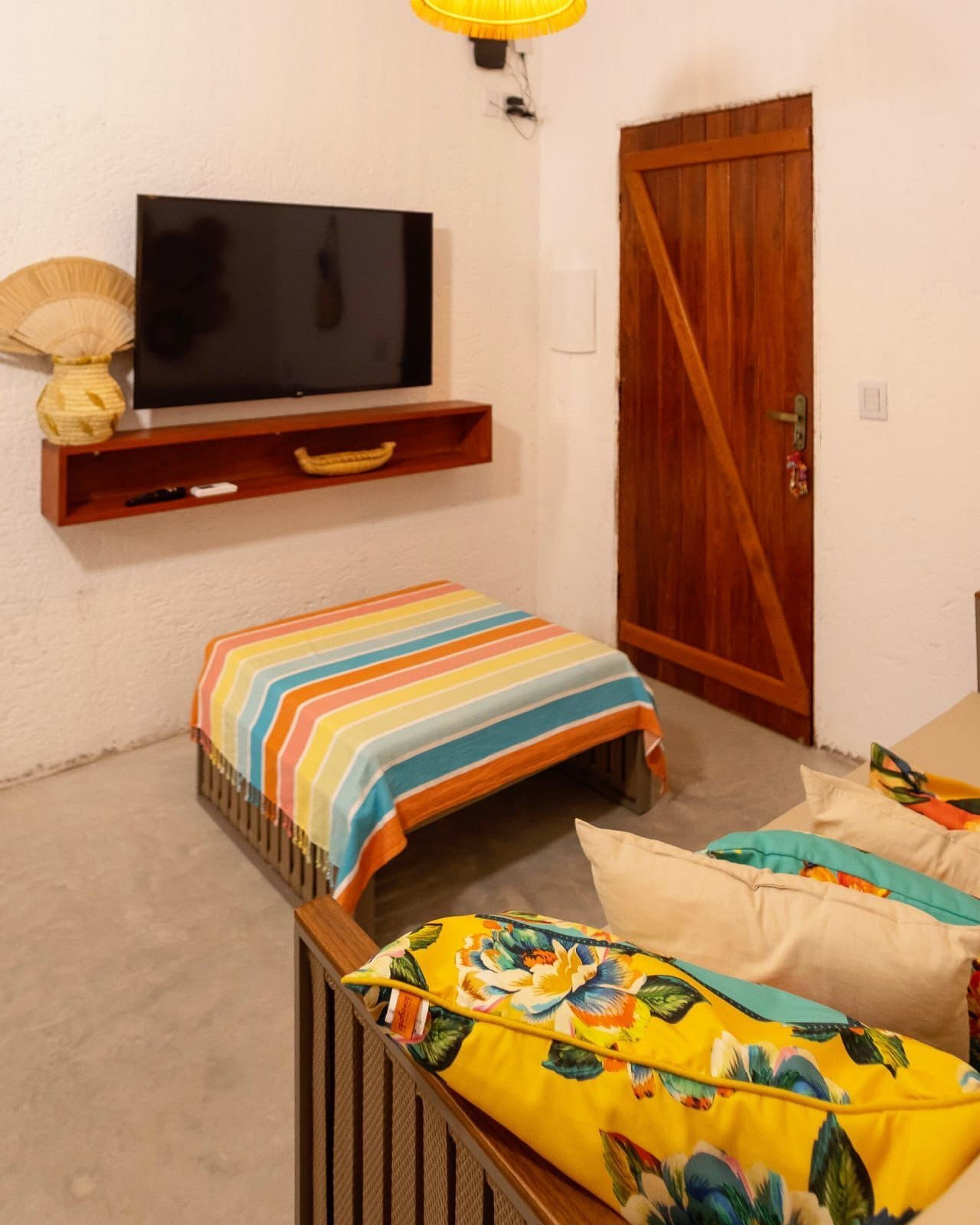 Una habitación pequeña y acogedora con televisión montada en la pared, una puerta de madera y una colcha de rayas coloridas.