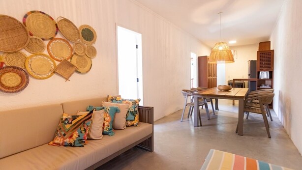 A modern living room with a sofa, a dining table, and chairs. There are woven baskets on the wall and a hanging light fixture. - MHV Milagres - Casa da Villa 08, Casa em Villa (Passo de Camaragibe)