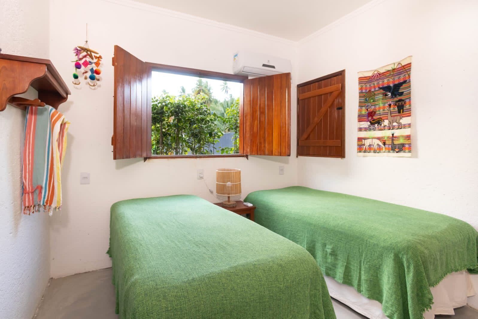A room with two beds, a window with wooden shutters, a wall-mounted air conditioner, and a colorful tapestry.