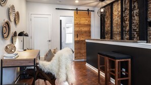 A modern interior with a wooden dining table, a fluffy white chair, and a rustic brick wall. - Romantic Designer Loft | Walk to Butler St! (Pittsburgh)