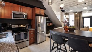 A modern kitchen with stainless steel appliances, wooden cabinets, and a central island with bar stools. - Romantic Designer Loft | Walk to Butler St! (Pittsburgh)