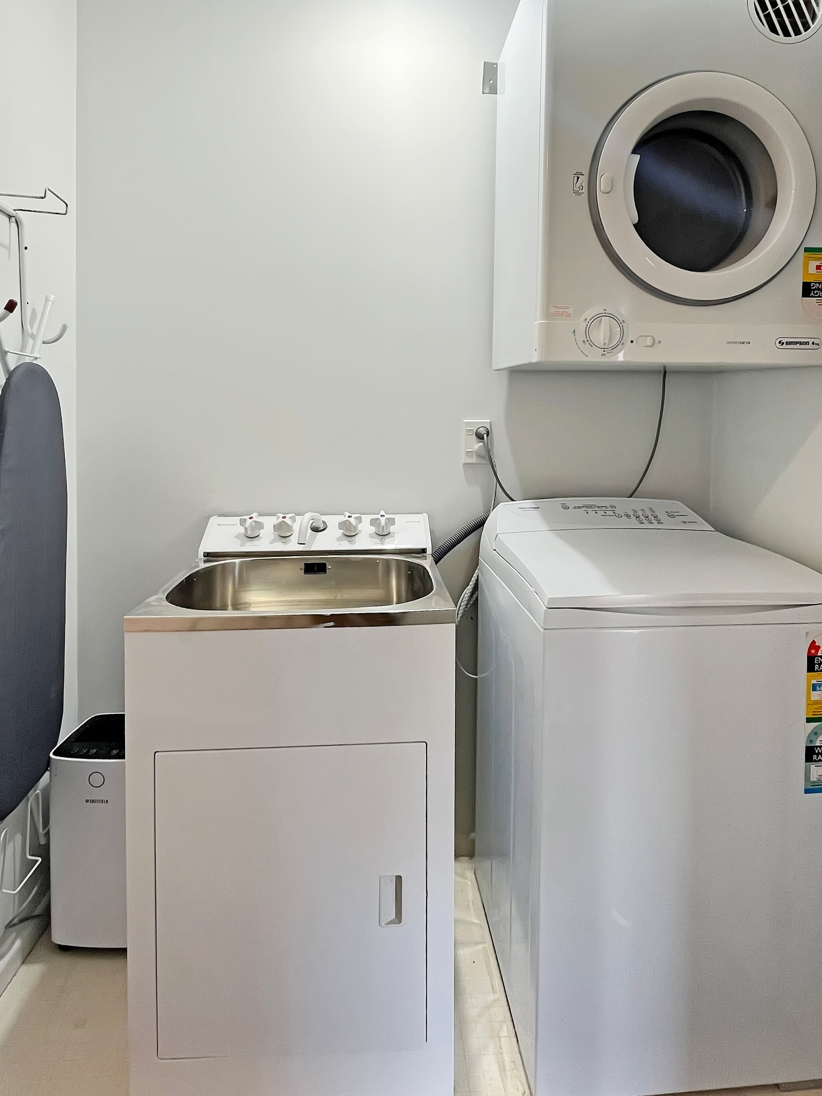 Un espace buanderie équipé d’un lave-linge et d’un sèche-linge à chargement frontal, d’un évier et d’un étendoir.