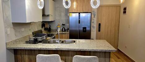 A modern kitchen with a granite countertop, stainless steel appliances, and two bar stools.