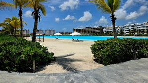 A resort with a pool, palm trees, and a sandy beach area. - Oasis Turquesa Punta Cana Crystal Lagoon (Punta Cana)