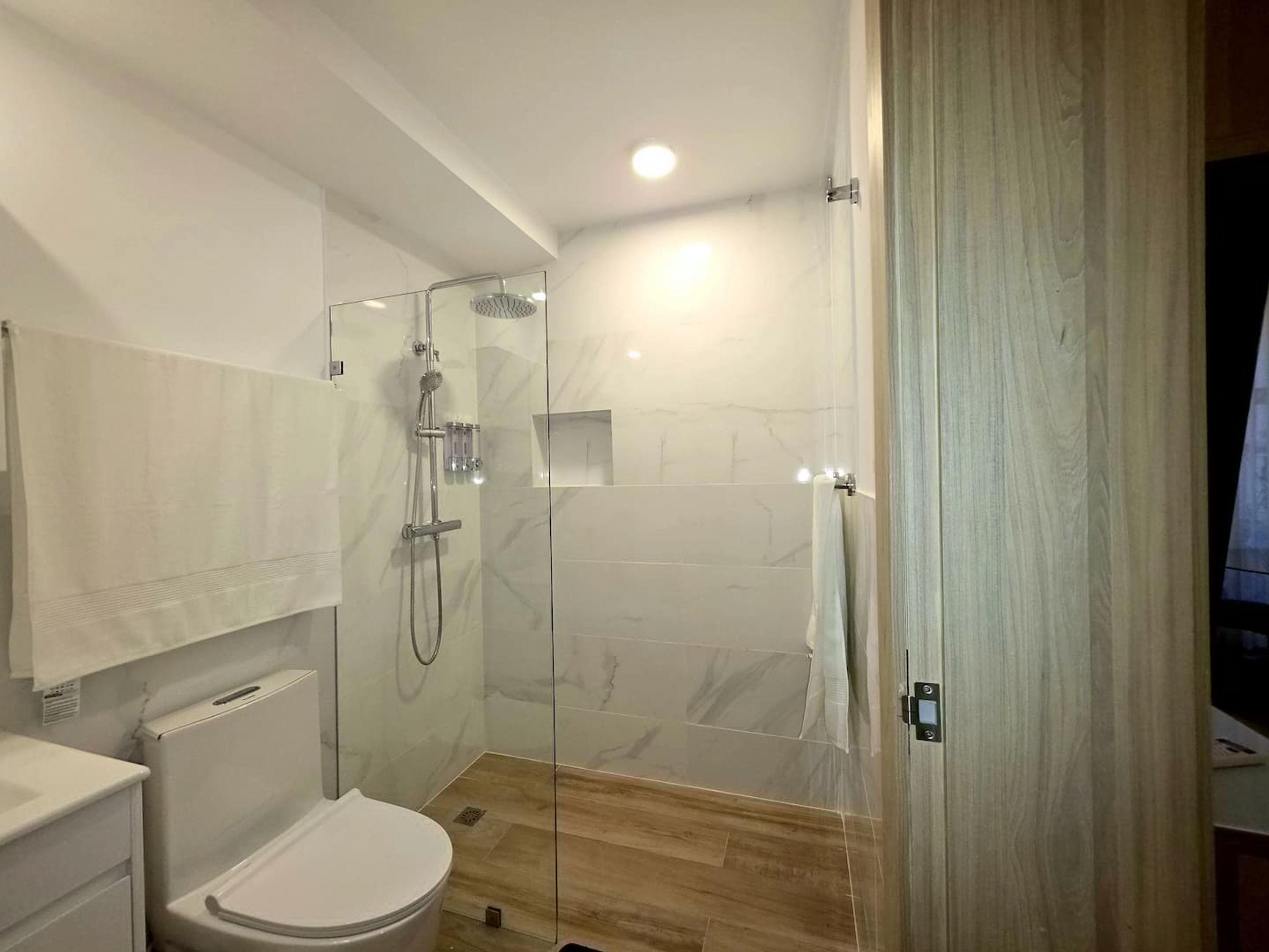 A modern bathroom with a glass-enclosed shower, a white toilet, and a wooden floor.