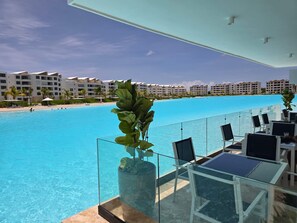 A poolside area with a glass railing, lounge chairs, and a potted plant. - Oasis Turquesa Punta Cana Crystal Lagoon (Punta Cana)
