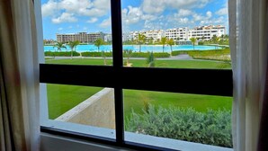 A view from a window overlooking a resort with multiple buildings, a swimming pool, and a well-maintained lawn. - Oasis Turquesa Punta Cana Crystal Lagoon (Punta Cana)
