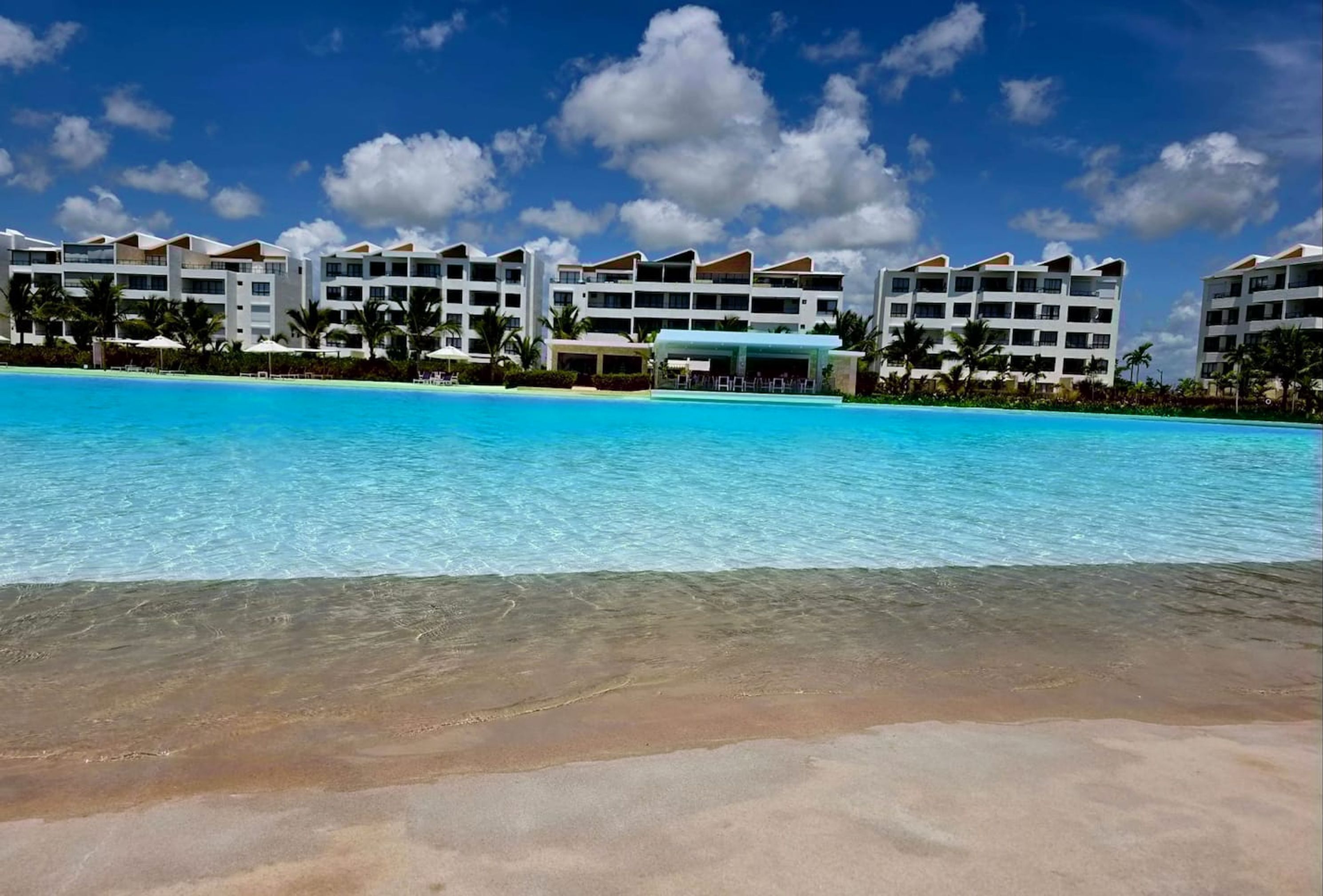 A resort with a large pool, multiple white buildings, and palm trees.