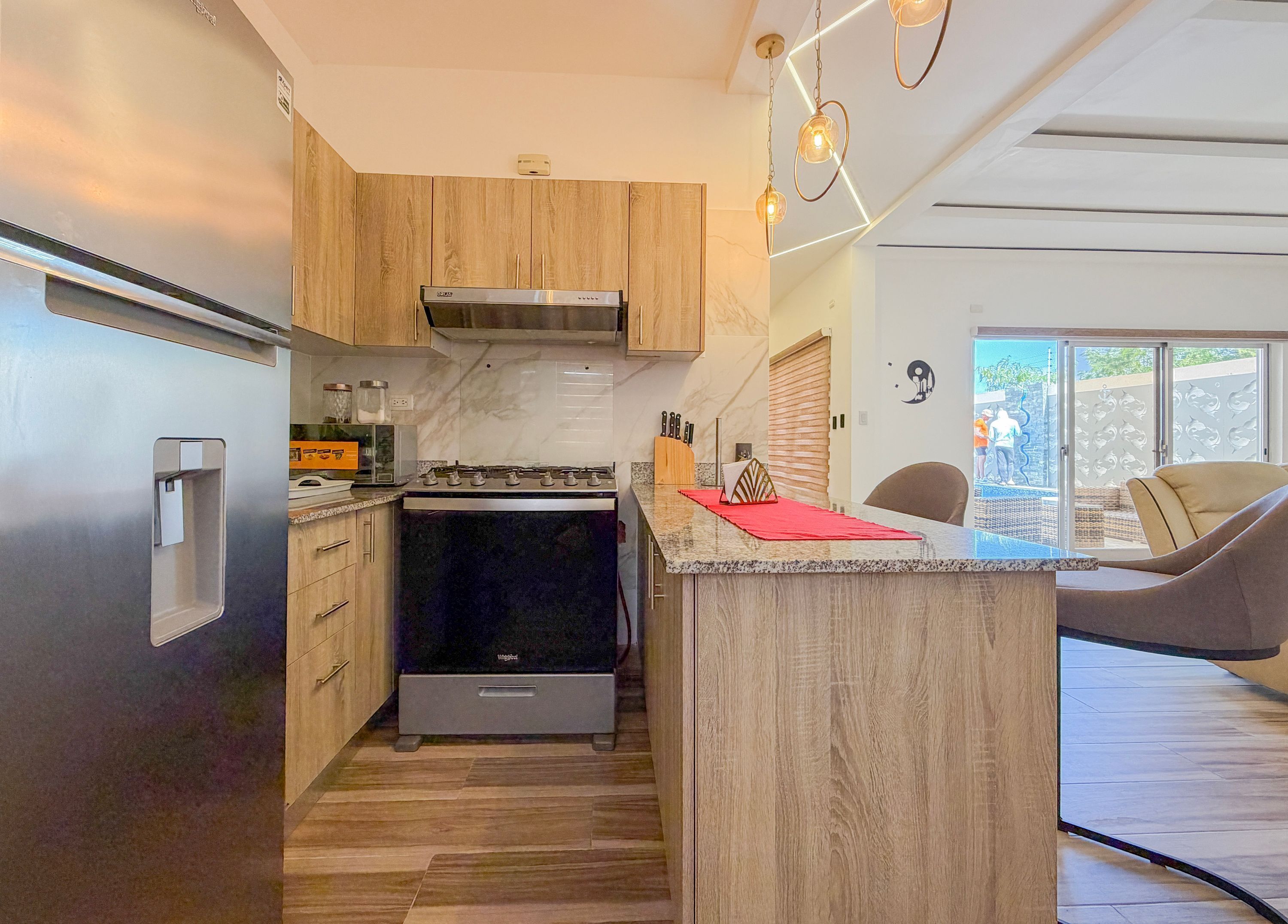 A modern kitchen with wooden cabinets, a built-in stove, and a red mat on the island.