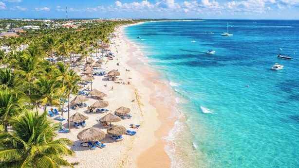 Une plage aux eaux turquoise et limpides, bordée de palmiers et parsemée de parasols.