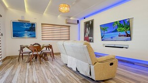Un salon moderne avec un plancher en bois, un canapé, une table à manger avec des chaises et des œuvres d’art accrochées aux murs.