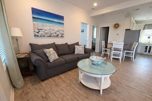 Ein Wohnzimmer mit einer Couch, einem Glastisch und einem Bild an der Wand.