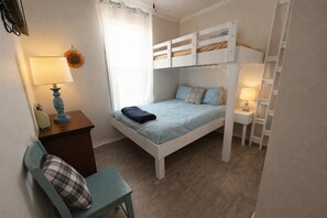 Ein Schlafzimmer mit Etagenbetten, einem Schreibtisch, einem Stuhl, einer Lampe und einem Fenster mit Vorhängen.