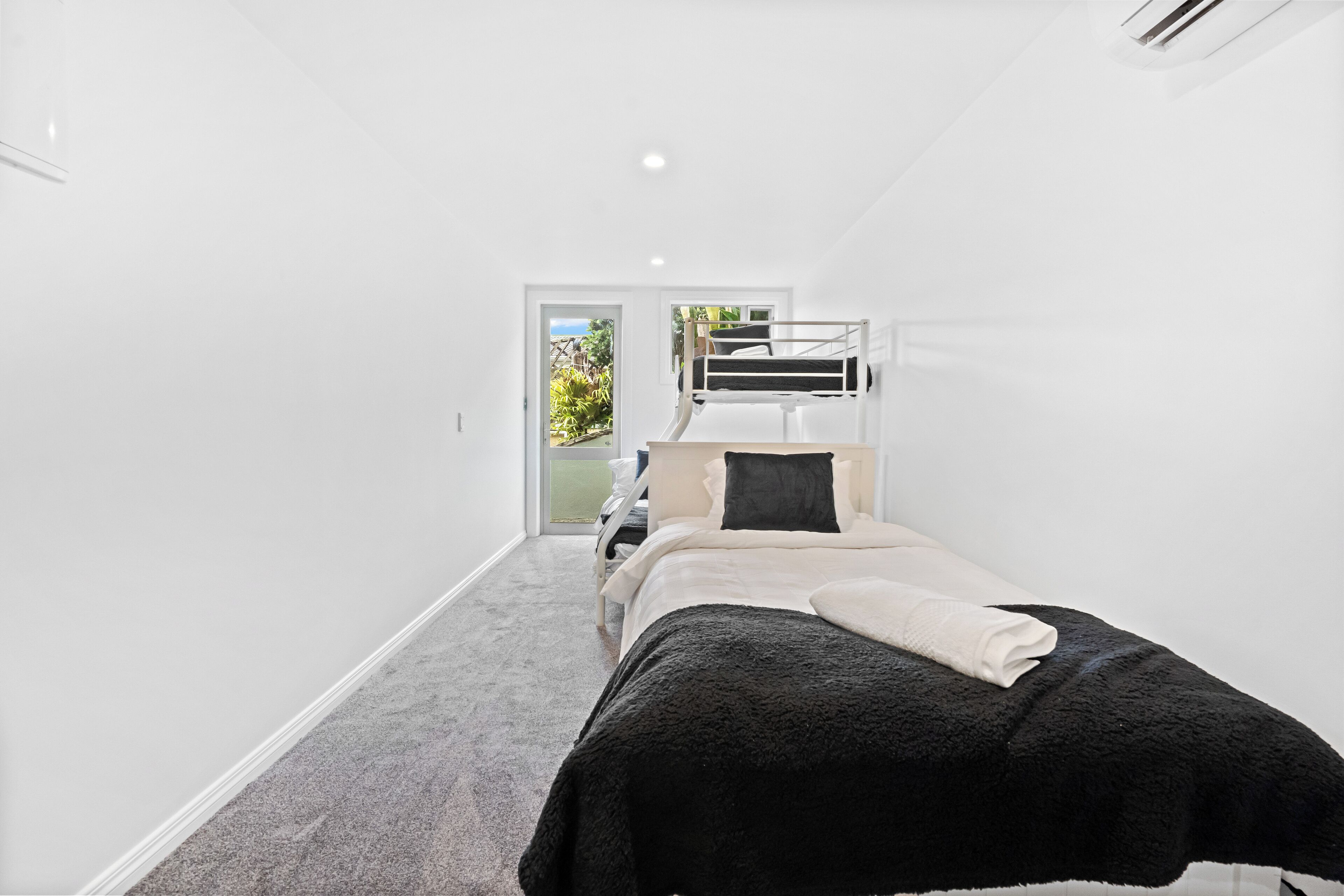 Ein Schlafzimmer mit Etagenbett, einer Tür, die auf einen Balkon führt, und Teppichboden.