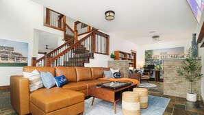 A spacious living room with a brown leather sectional sofa, a wooden staircase, and a stone fireplace. - Lion’s Lookout | PSU Retreat w/Hot Tub & Game Room (Bellefonte)